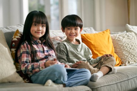 Photo for Portrait of two asian children brother and sister sitting on family couch at home looking at camera smiling - Royalty Free Image