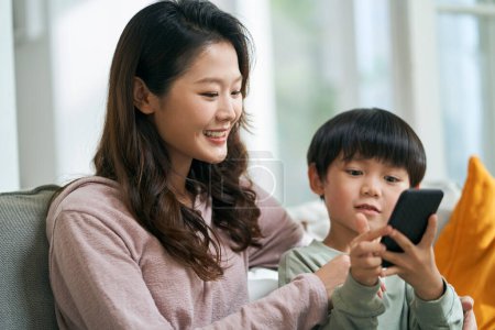 Photo for Young asian woman mother sitting on family couch keeping company with five-year-old son - Royalty Free Image