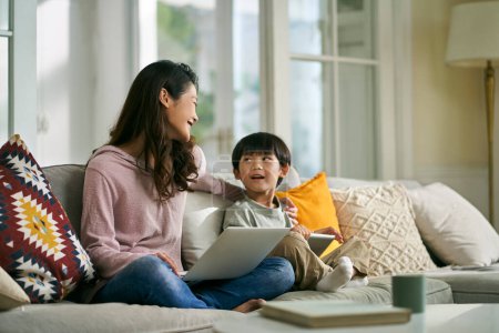 Photo for Young asian mother and five-year-old son sitting on couch at home having a pleasant conversation - Royalty Free Image