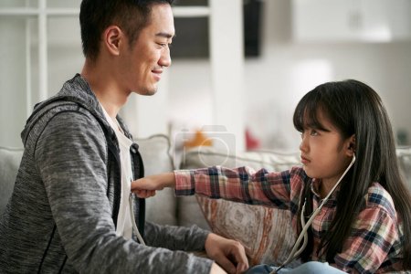 Foto de Joven asiático padre jugando médico y paciente juego con siete años de edad, hija en casa - Imagen libre de derechos