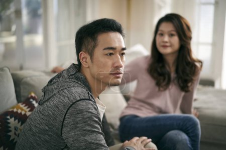 Photo for Young asian couple sitting on family couch at home talking through their marriage problems - Royalty Free Image