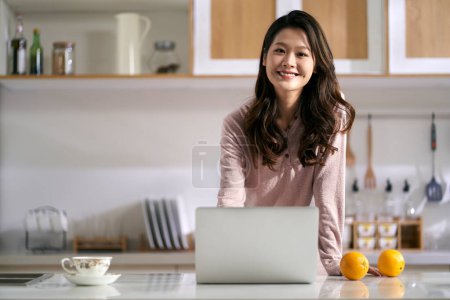Photo for Portrait of a happy successful woman female freelancer standing behind kitchen counter at home looking at camera smiling - Royalty Free Image