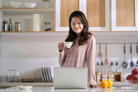 Photo for Young asian business woman female freelancer working in kitchen at home using laptop computer - Royalty Free Image