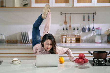 Photo for Young asian business woman female freelancer stretching legs while working in kitchen at home using laptop computer - Royalty Free Image