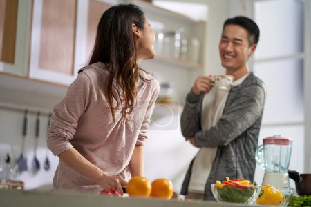 Photo for Happy loving young asian couple chatting while preparing meal together in kitchen at home - Royalty Free Image