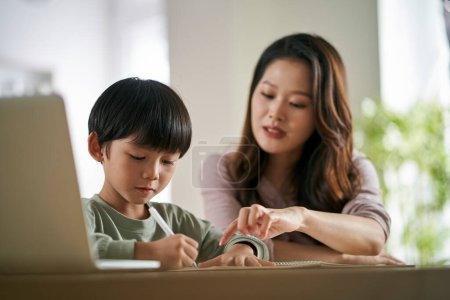 Photo for Young asian mother sitting at table at home helping son with his study - Royalty Free Image