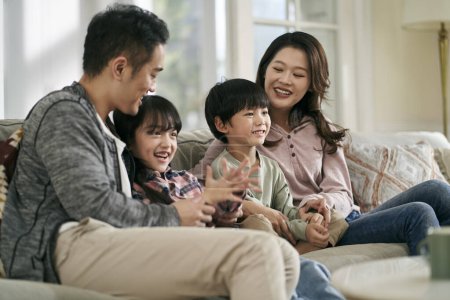 Photo for Happy asian family with two children sitting on couch at home watching tv together - Royalty Free Image