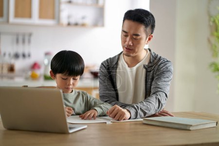 Photo for Young asian father sitting at table tutoring son at home - Royalty Free Image