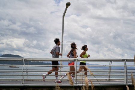 Téléchargez les photos : Groupe de trois asiatique jeune adulte homme et femme courir jogging en plein air dans parc par la mer - en image libre de droit