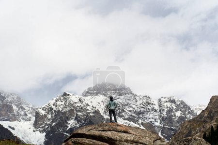 Téléchargez les photos : Vue arrière de l'homme asiatique voyageur masculin debout sur un rocher regardant une montagne de neige dans le Xinjiang, en Chine - en image libre de droit