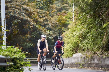 Téléchargez les photos : Jeune asiatique couple cyclistes équitation vélo sur la route rurale - en image libre de droit