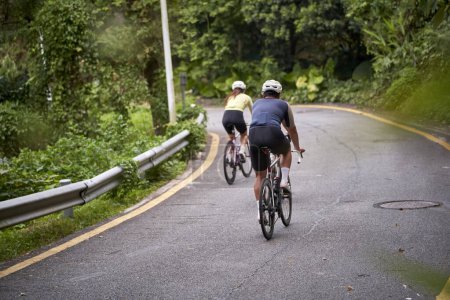 Foto de Vista trasera de jóvenes asiáticos pareja ciclistas montar en bicicleta en carretera rural - Imagen libre de derechos