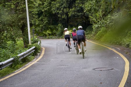 Foto de Vista trasera del grupo de tres jóvenes ciclistas adultos asiáticos montar en bicicleta al aire libre en la carretera rural - Imagen libre de derechos