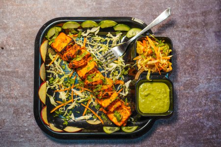 Téléchargez les photos : Paneer tikka est un plat indien à base de morceaux de paneer avec sauce et légumes sur la table - en image libre de droit