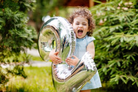 Muy feliz niña de dos años celebrando su cumpleaños, riendo, sosteniendo el número del globo. Humor de cumpleaños