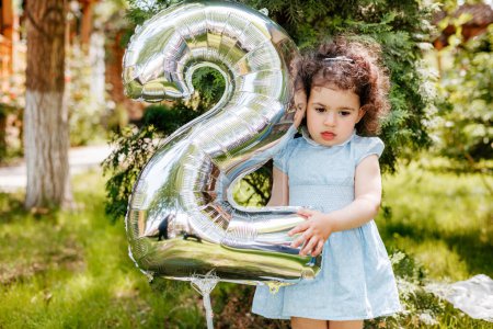 Thoughtful face of cute curly hair girl holding her birthday number two balloon