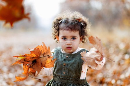 Close up of astonished child holding crisp leaves, standing in a world of fallen foliage.