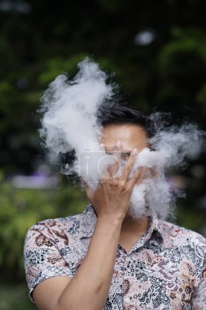 Téléchargez les photos : Gros plan d'un jeune homme expirant un nuage de vapeur ou de fumée à l'aide d'une cigarette électronique - en image libre de droit