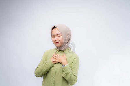 Feliz consciente agradecida joven mujer musulmana asiática con su mano en el pecho sonriendo aislada sobre fondo blanco