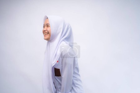 Téléchargez les photos : Heureuse étudiante indonésienne du secondaire en uniforme blanc et gris sur Copy Space Advertising Your Text, debout isolé sur fond de studio blanc - en image libre de droit