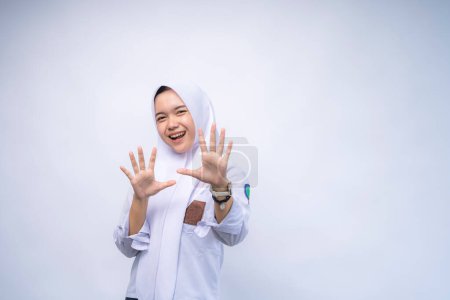 Überraschte indonesische Gymnasiastin in weiß-grauer Uniform schreit, während sie vor weißem Hintergrund in die Kamera blickt