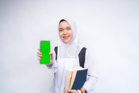 Una estudiante de secundaria indonesia emocionada con uniforme blanco y gris apuntando al espacio de copia en su teléfono inteligente en la mano, aislada sobre fondo blanco