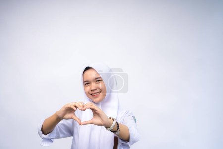 Weibliche indonesische High-School-Studentin in weiß-grauer Uniform macht Herz mit Fingern oder Dreieck Zeichen isoliert weißen Hintergrund