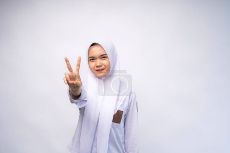 Excited Female Indonesian high school student in white and grey uniform giving number two by hand gesture