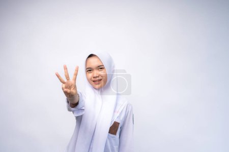 Excited Female Indonesian high school student in white and grey uniform giving number three by hand gesture