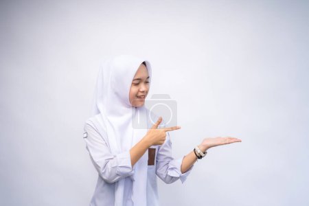 Aufgeregt zeigt eine indonesische Gymnasiastin in weiß-grauer Uniform auf den Kopierraum neben ihr, abgeschirmt von weißem Hintergrund.