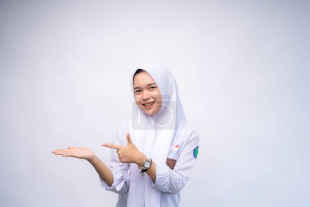 Aufgeregt zeigt eine indonesische Gymnasiastin in weiß-grauer Uniform auf den Kopierraum neben ihr, abgeschirmt von weißem Hintergrund.