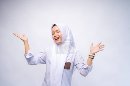 Téléchargez les photos : Heureuse étudiante indonésienne du secondaire en uniforme blanc et gris sur Copy Space Advertising Your Text, debout isolé sur fond de studio blanc - en image libre de droit
