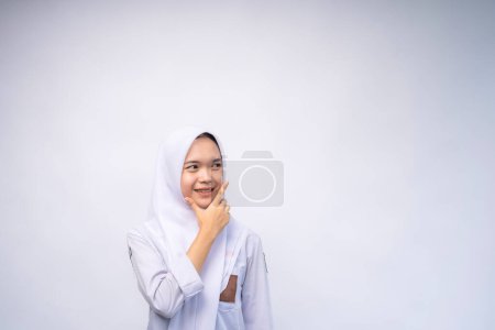 Glückliche indonesische Gymnasiastin in weiß-grauer Uniform bei Copy Space Advertising Your Text, stehend isoliert über weißem Studiohintergrund