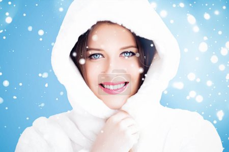 Foto de Felices fiestas, belleza y moda de invierno, hermosa mujer con abrigo de piel esponjosa blanca, nieve nevando sobre fondo azul como Navidad, Año Nuevo y estilo de vida de vacaciones estilo retrato - Imagen libre de derechos