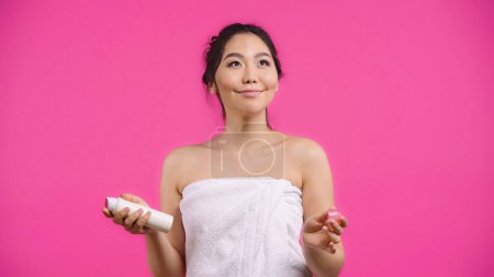 Téléchargez les photos : Asiatique jeune femme en serviette tenant déodorant et souriant isolé sur rose - en image libre de droit