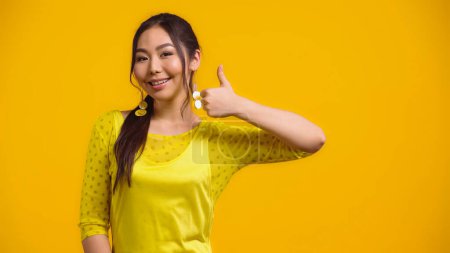 Téléchargez les photos : Heureux asiatique femme montrant pouce vers le haut et sourire isolé sur jaune - en image libre de droit