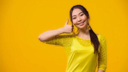 Téléchargez les photos : Positif asiatique jeune femme montrant pouce vers le haut isolé sur jaune - en image libre de droit