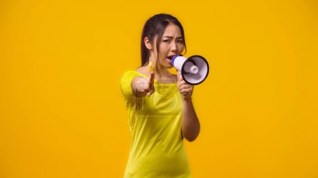 unzufriedene asiatische Frau schreit in Megafon und zeigt mit dem Finger isoliert auf gelb 
