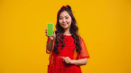 Téléchargez les photos : Heureux asiatique femme tenant smartphone avec écran vert isolé sur jaune - en image libre de droit