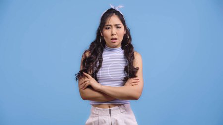 Photo for Dissatisfied asian woman in crop top standing with crossed arms isolated on blue - Royalty Free Image