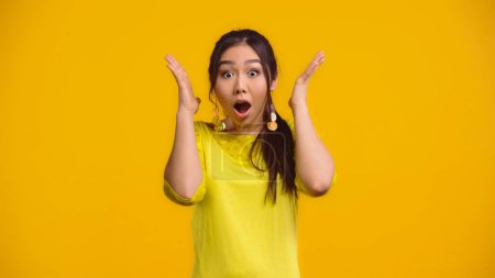 shocked asian woman with opened mouth gesturing isolated on yellow  