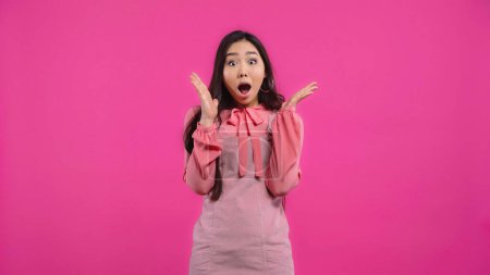 schockierte asiatische Frau mit geöffnetem Mund gestikuliert isoliert auf rosa