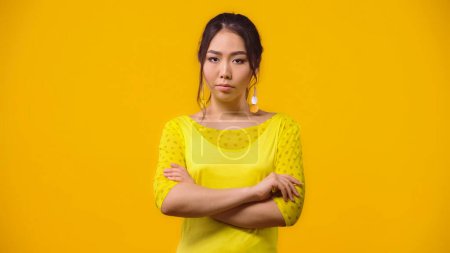 Foto de Mujer asiática insatisfecha de pie con los brazos cruzados aislados en amarillo - Imagen libre de derechos