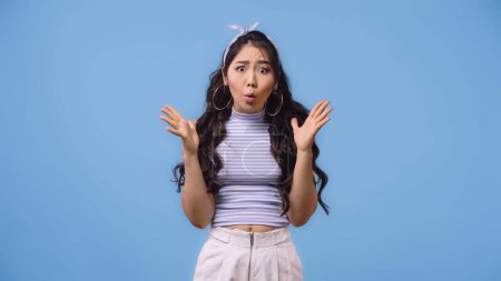 shocked and young asian woman with opened mouth gesturing isolated on blue 