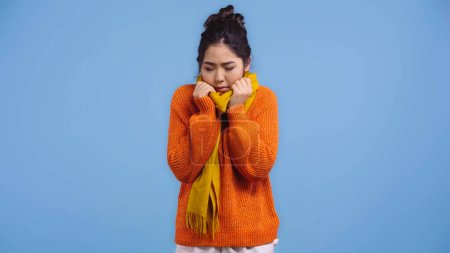 enfermo asiático mujer en naranja suéter y bufanda sensación frío aislado en azul 