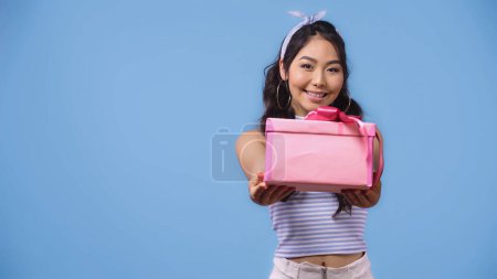 Photo for Positive asian woman giving wrapped present isolated on blue - Royalty Free Image