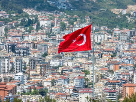 Photo for Alanya, Turkey - Apr 26, 2023. The Turkish flag proudly flying over a modern Alanya city. The view from Alanya fortress, with some thermal fluctuations in air - Royalty Free Image