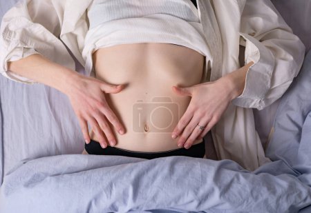 Photo for Healthy nutrition and belly health concept. Close up of woman flat stomach. Girl in bed with hungry feeling. Top view - Royalty Free Image