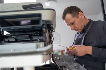 técnico de reparación de impresoras. Un manitas masculino inspecciona una impresora antes de comenzar las reparaciones en el apartamento de un cliente.