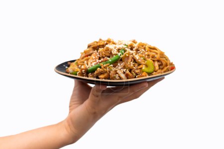 Téléchargez les photos : Faire revenir les nouilles udon avec du porc et des légumes colorés dans un plat noir isolé sur fond blanc. Cuisine asiatique. - en image libre de droit